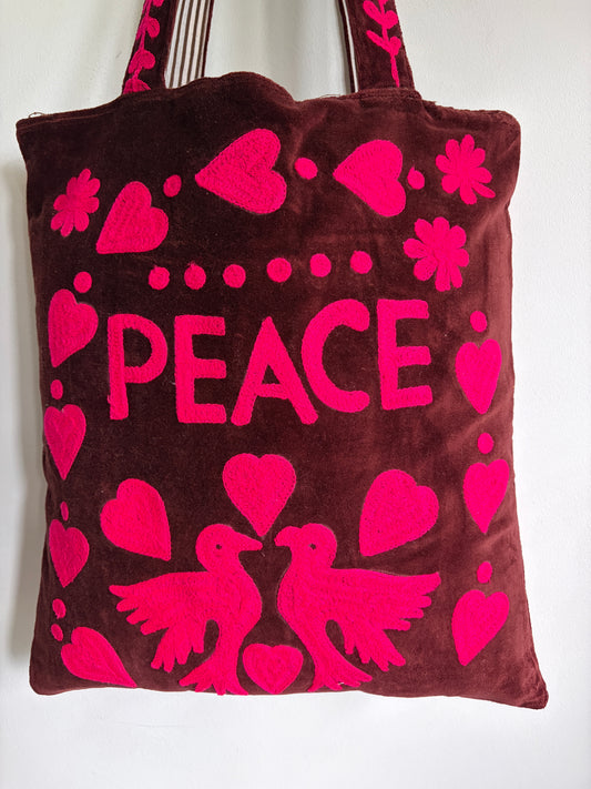 Brown tote bag with pink 'PEACE' text and heart designs on a plain background