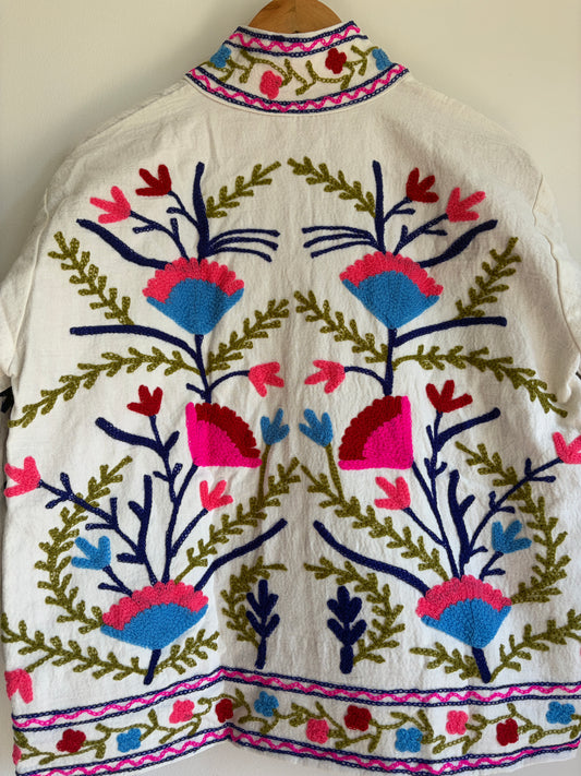 Colorful embroidered jacket on a hanger against a white background