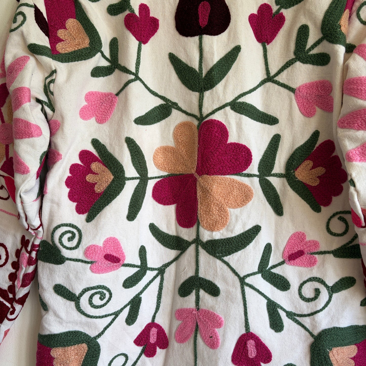 White quilted jacket with pink, green, and black embroidered paisley and floral patterns.