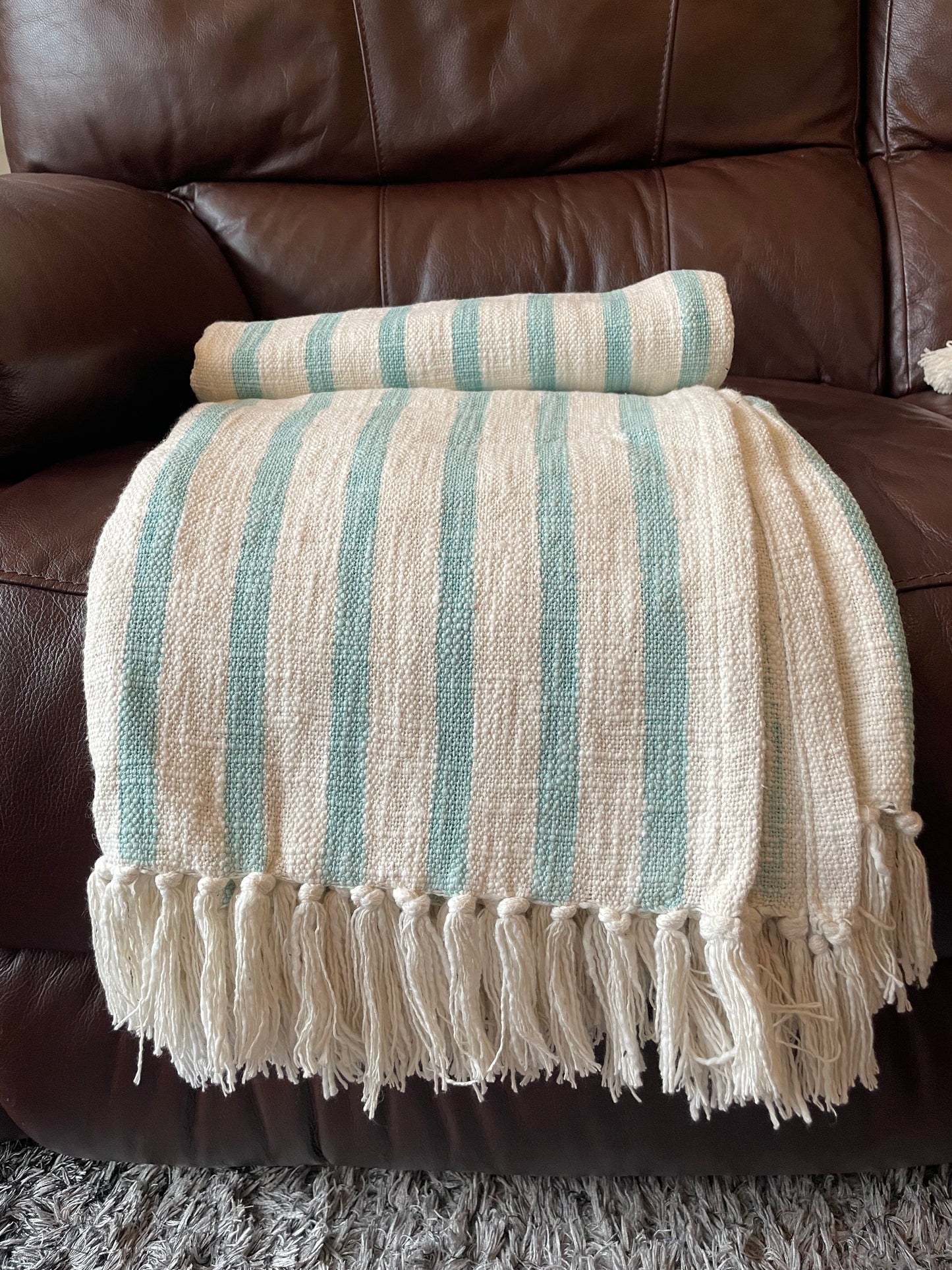 Striped blanket with tassels draped over a brown leather sofa.