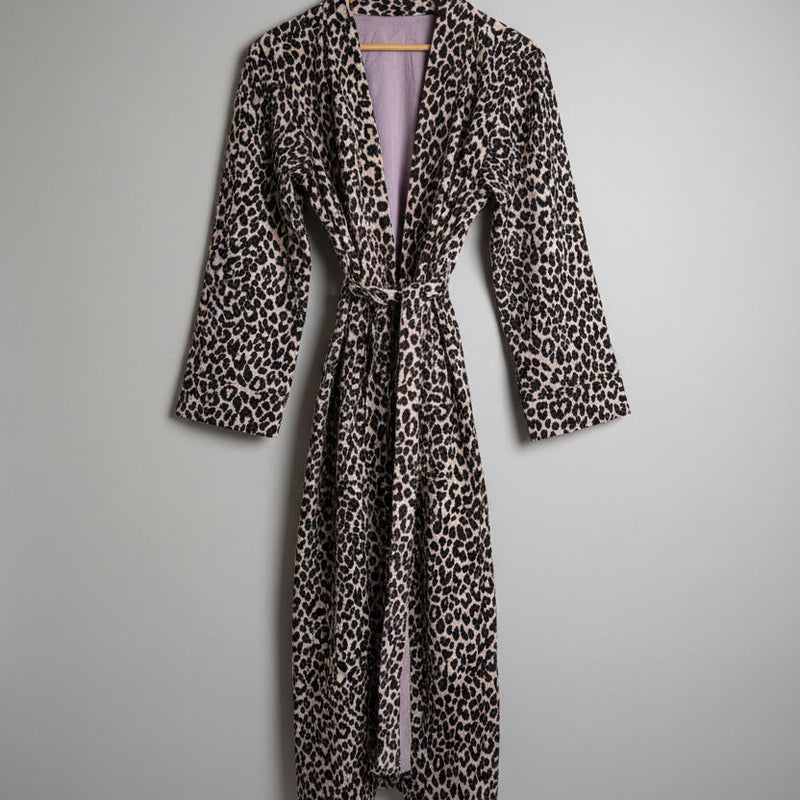 A leopard print robe hanging on a hanger against a plain white wall. 
