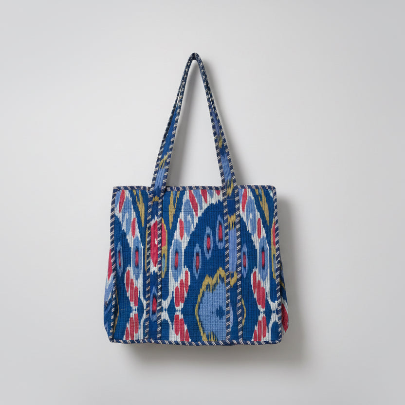 Colorful patterned bag hanging on a white window frame with green plants.