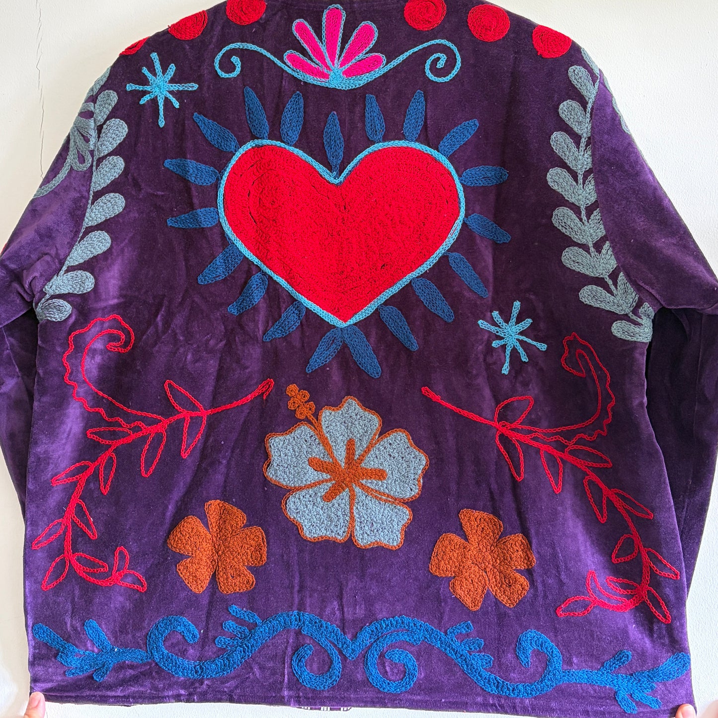 Purple fabric with colorful embroidered patterns on a white background