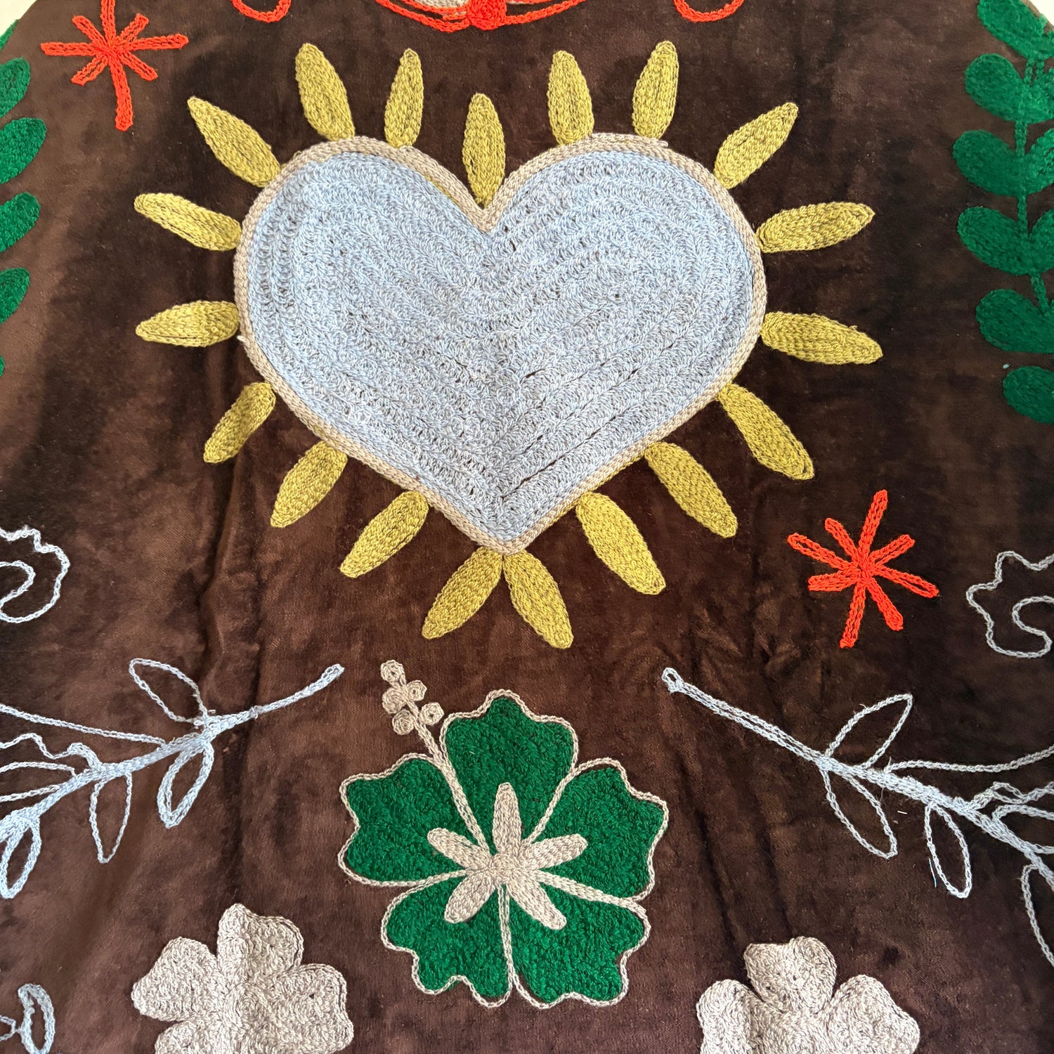 Decorative fabric with embroidered heart, flowers, and leaves on a brown background