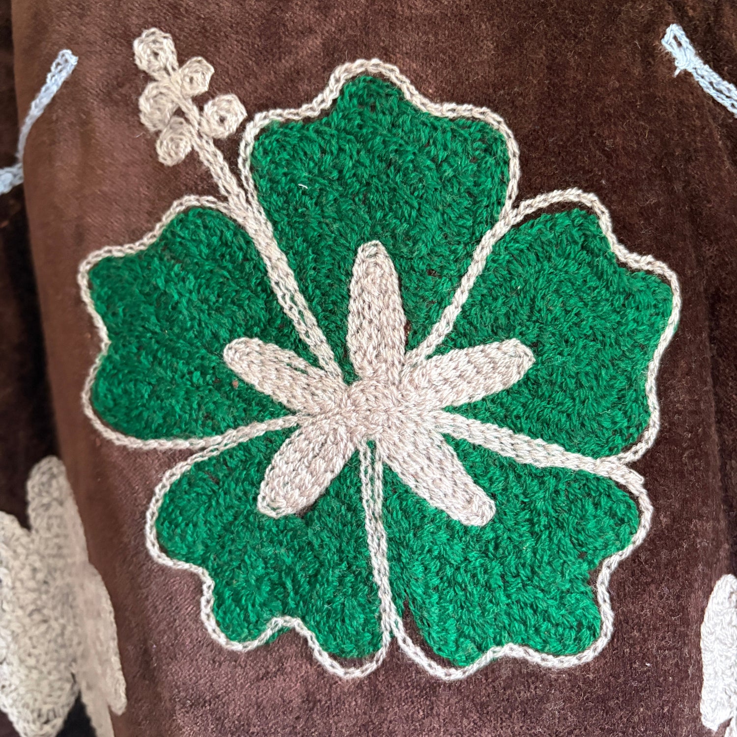 Embroidered green clover design on a brown fabric background