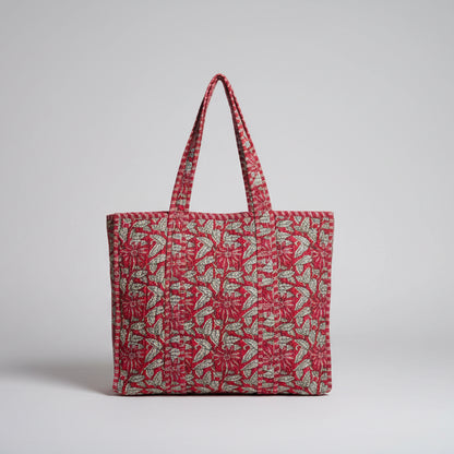 Red patterned bag on a white surface with green leaves