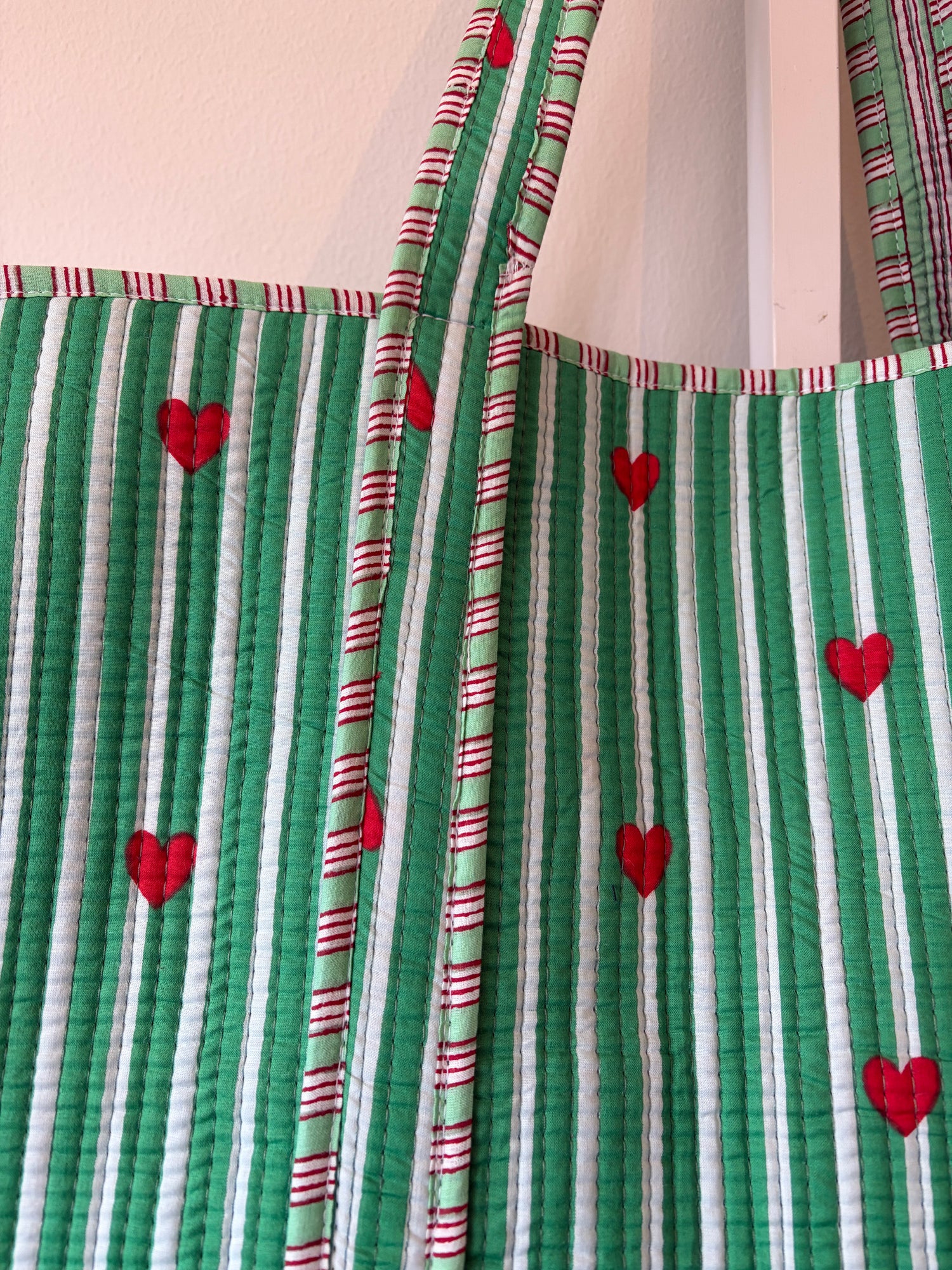 Close-up of green and white striped bag with red heart patterns on a beige surface.