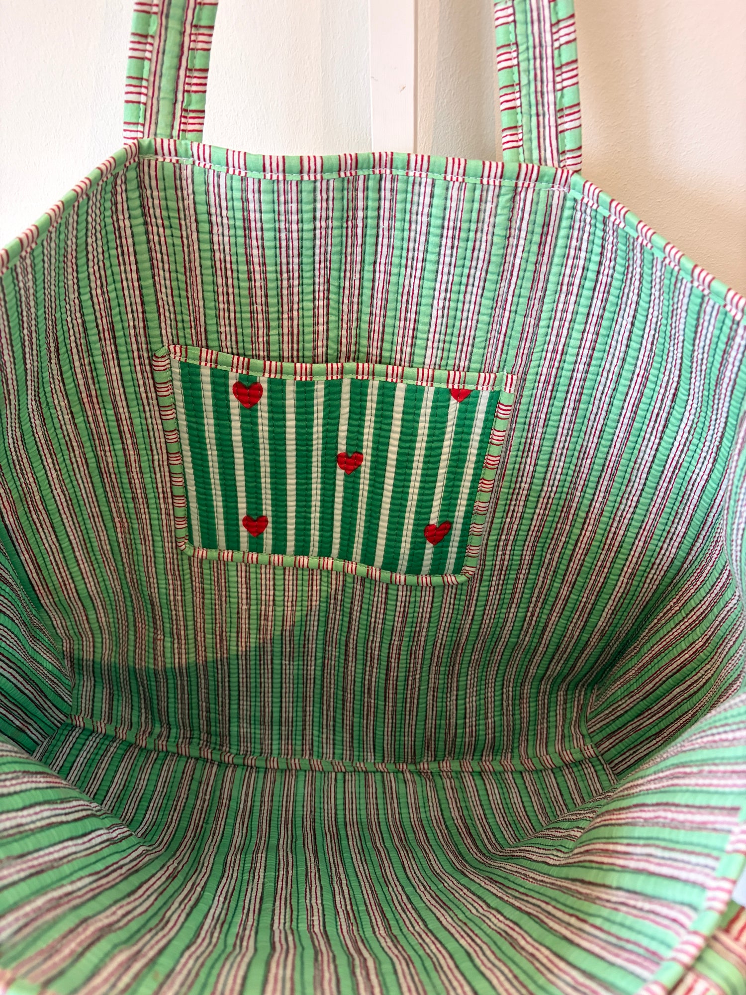 Close-up of a green and red striped tote bag with a pocket and buttons.