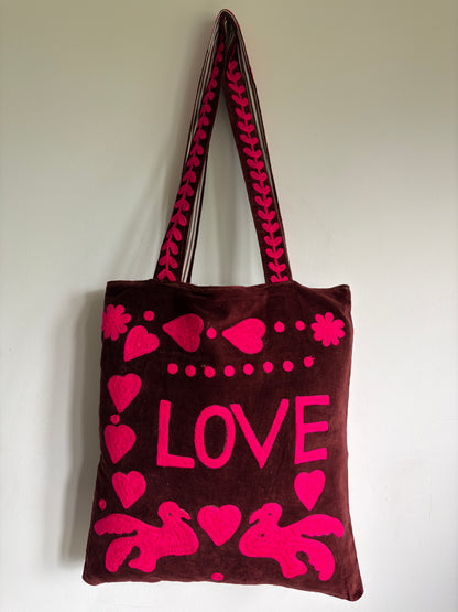 Brown tote bag with pink 'PEACE' text and heart designs on a plain background