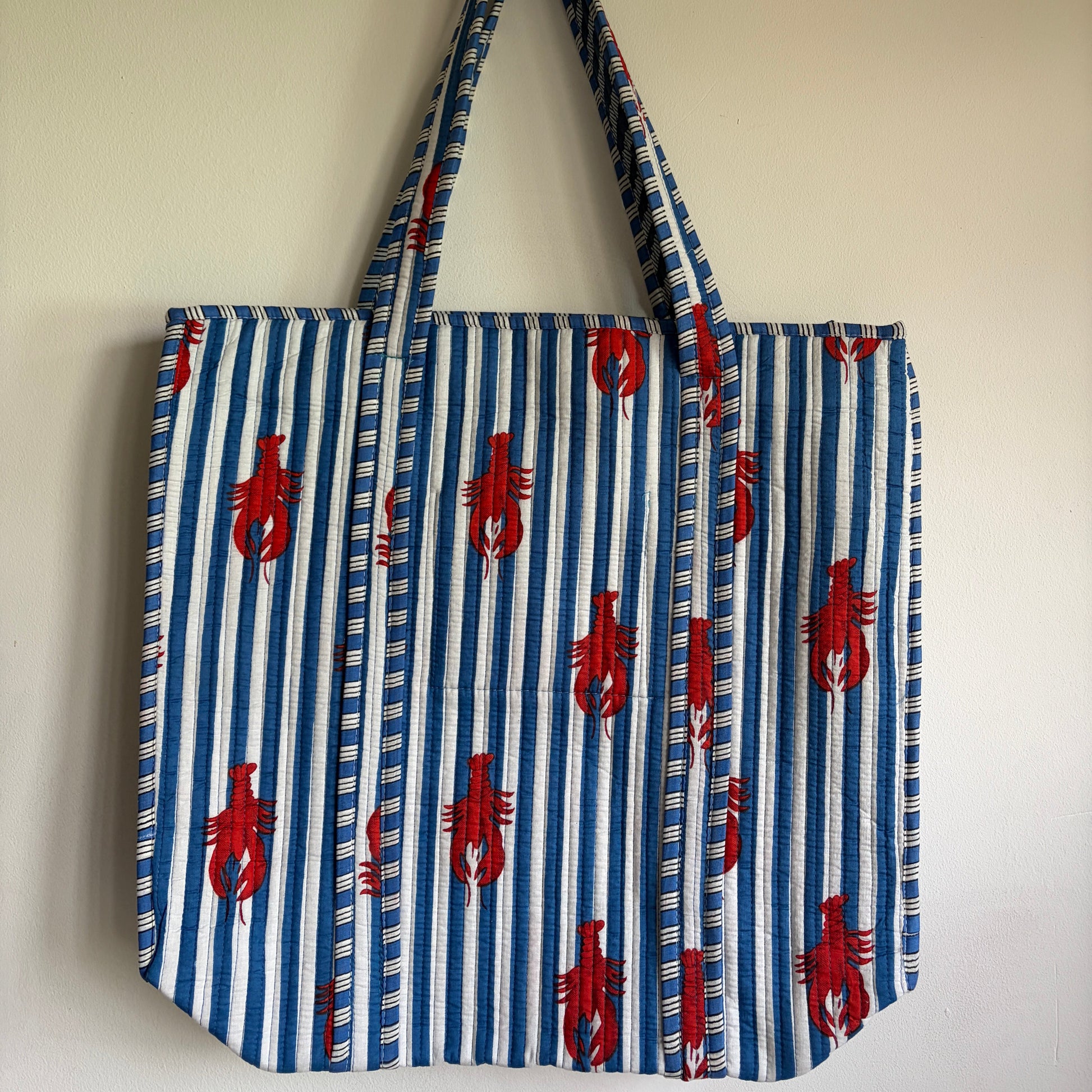 Blue and white striped bag with red lobster patterns on a beige background