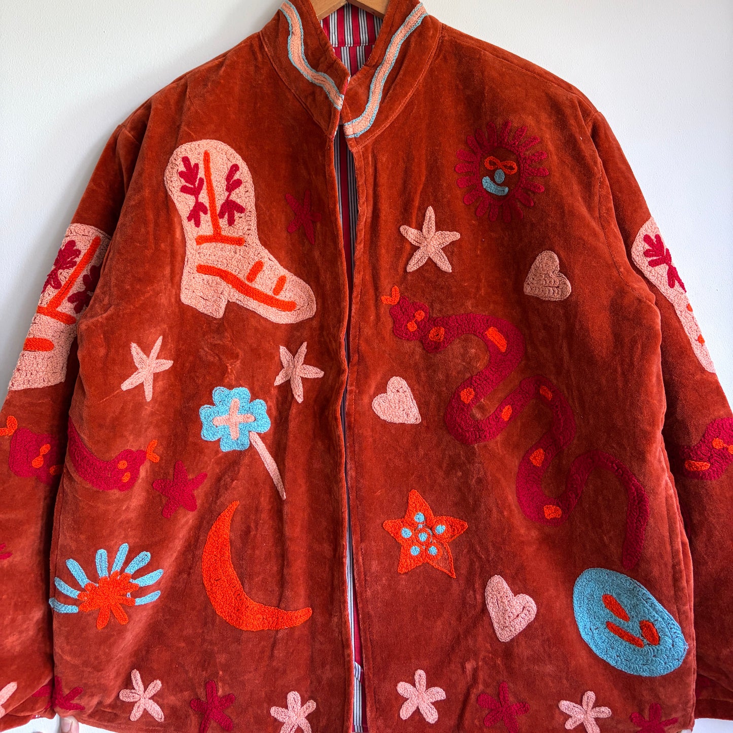 Suzani jacket with colorful patterns on a hanger against a white wall