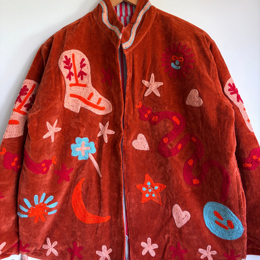 Suzani jacket with colorful patterns on a hanger against a white wall
