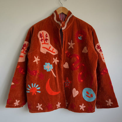 Suzani jacket with colorful patterns on a hanger against a white wall