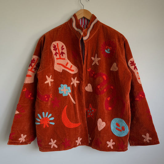 Suzani jacket with colorful patterns on a hanger against a white wall