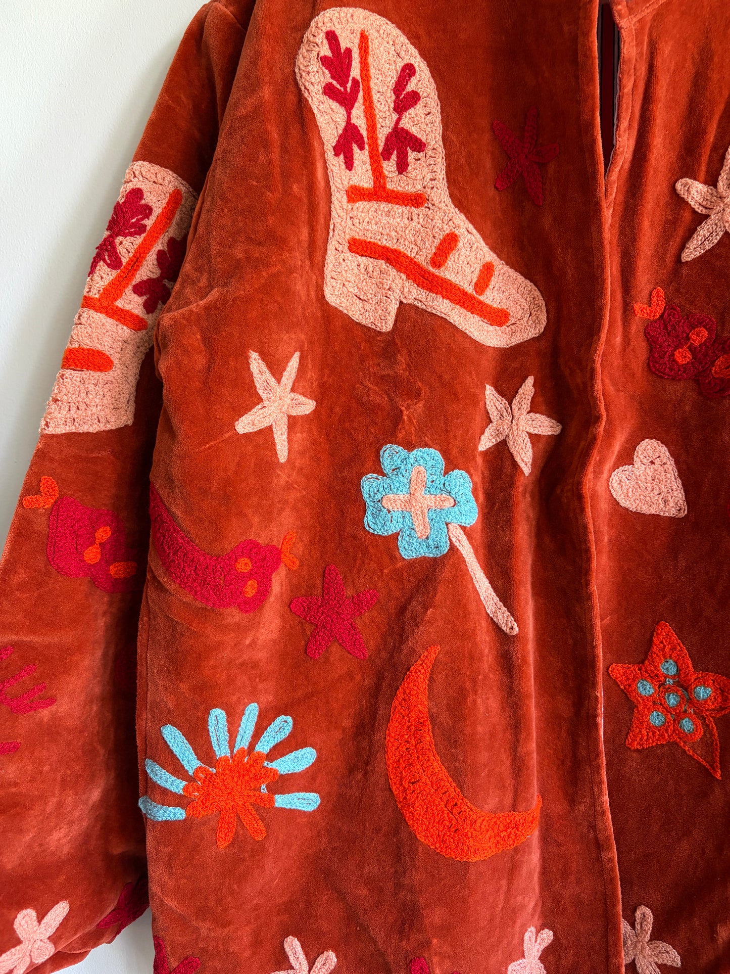 Suzani jacket with colorful patterns on a hanger against a white wall