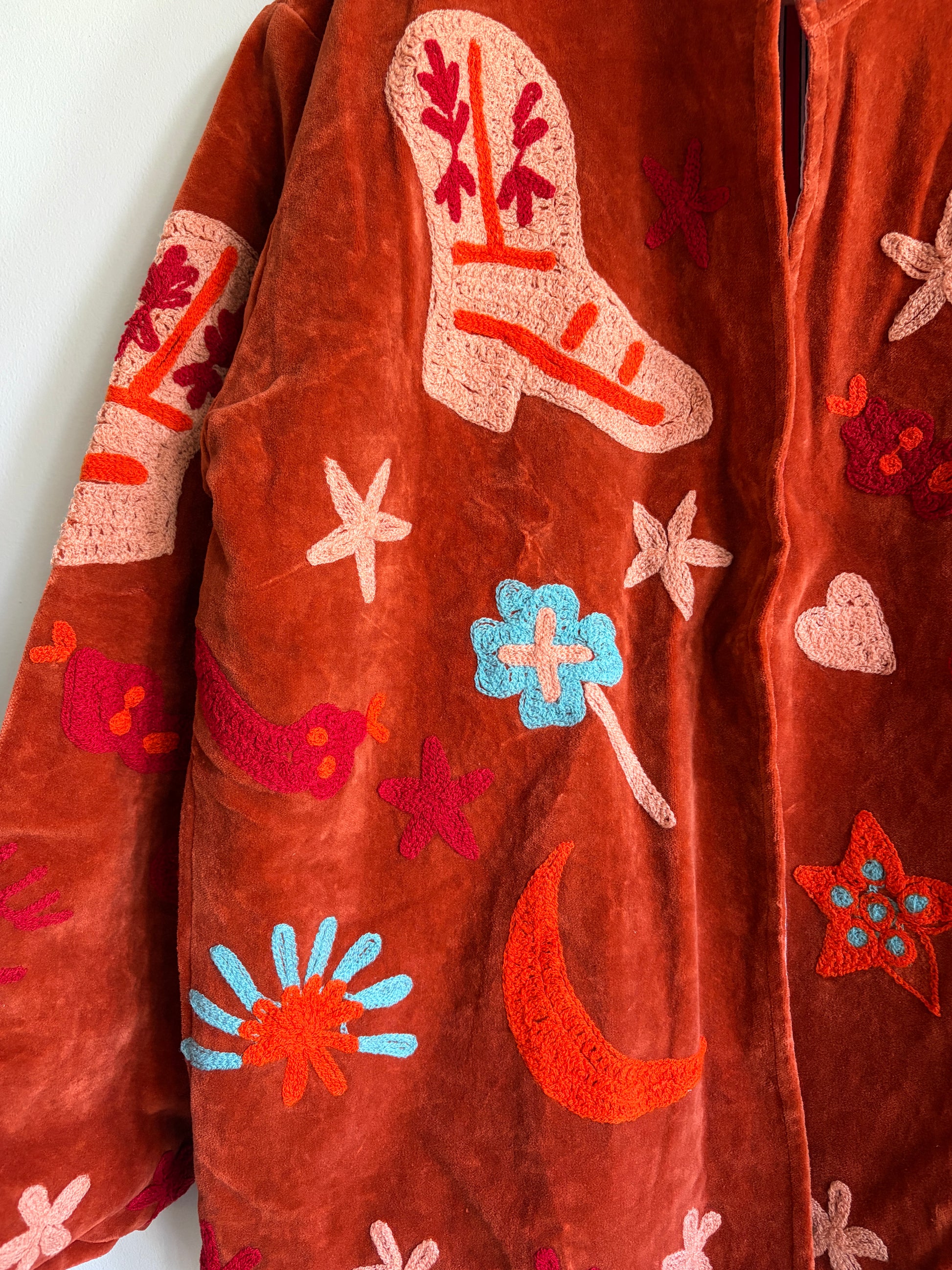 Suzani jacket with colorful patterns on a hanger against a white wall
