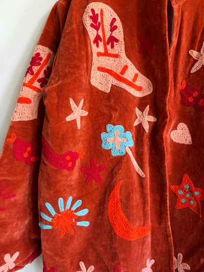 Suzani jacket with colorful patterns on a hanger against a white wall