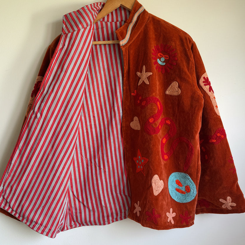 Suzani jacket with colorful patterns on a hanger against a white wall