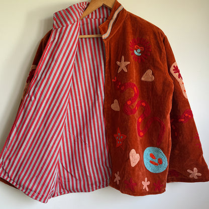Suzani jacket with colorful patterns on a hanger against a white wall