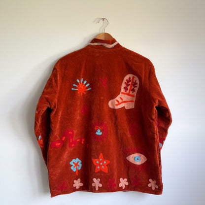 Suzani jacket with colorful patterns on a hanger against a white wall