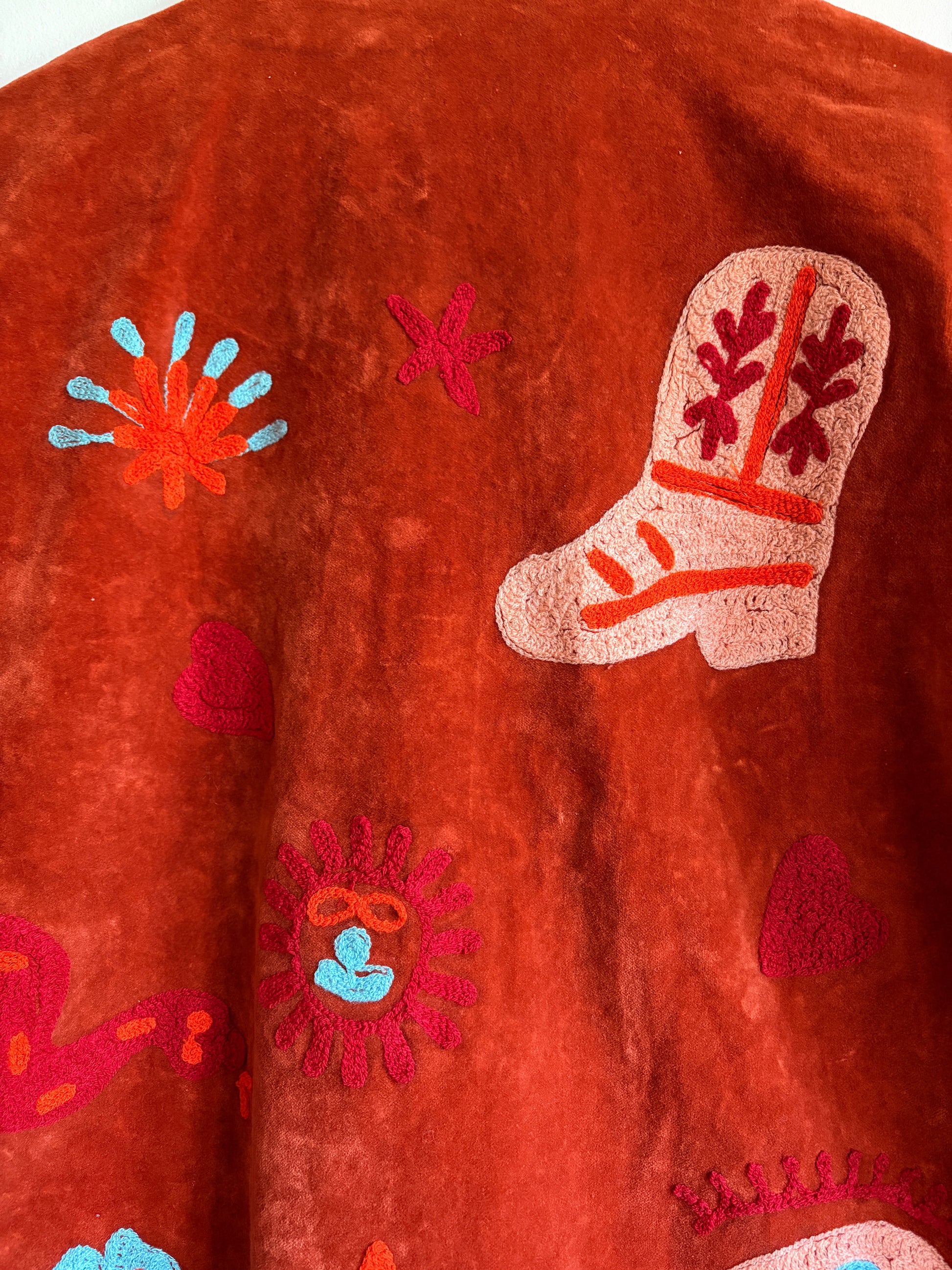 Suzani jacket with colorful patterns on a hanger against a white wall