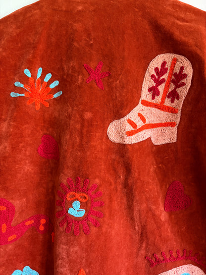 Suzani jacket with colorful patterns on a hanger against a white wall