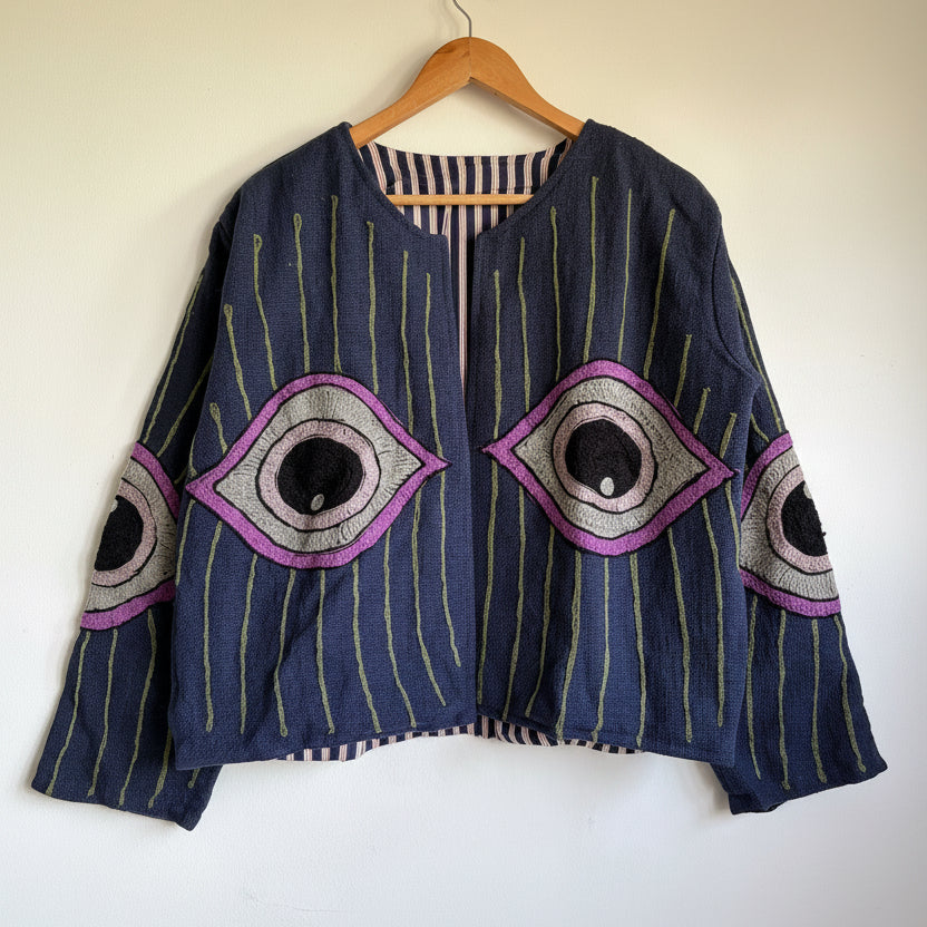 Blue suzani jacket with purple and gray geometric patterns on a beige background