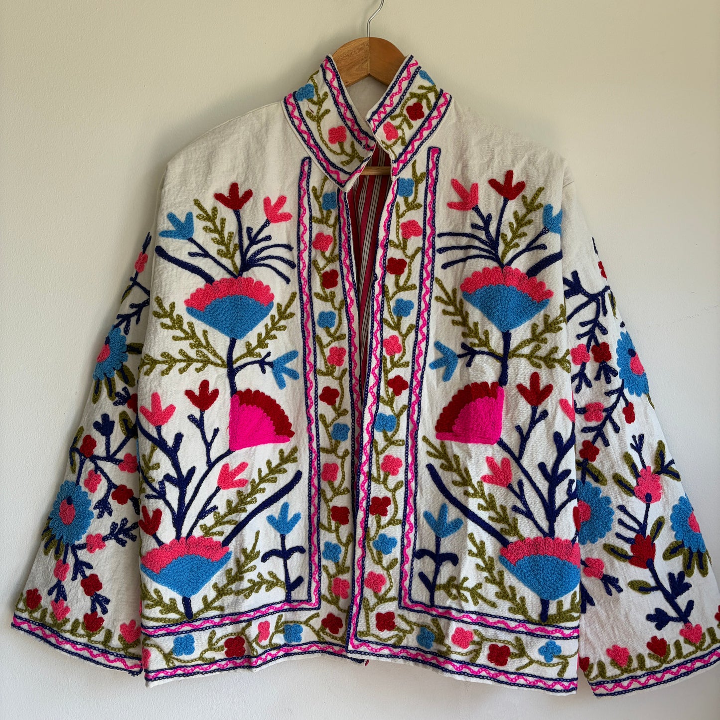 Colorful embroidered jacket on a hanger against a white background