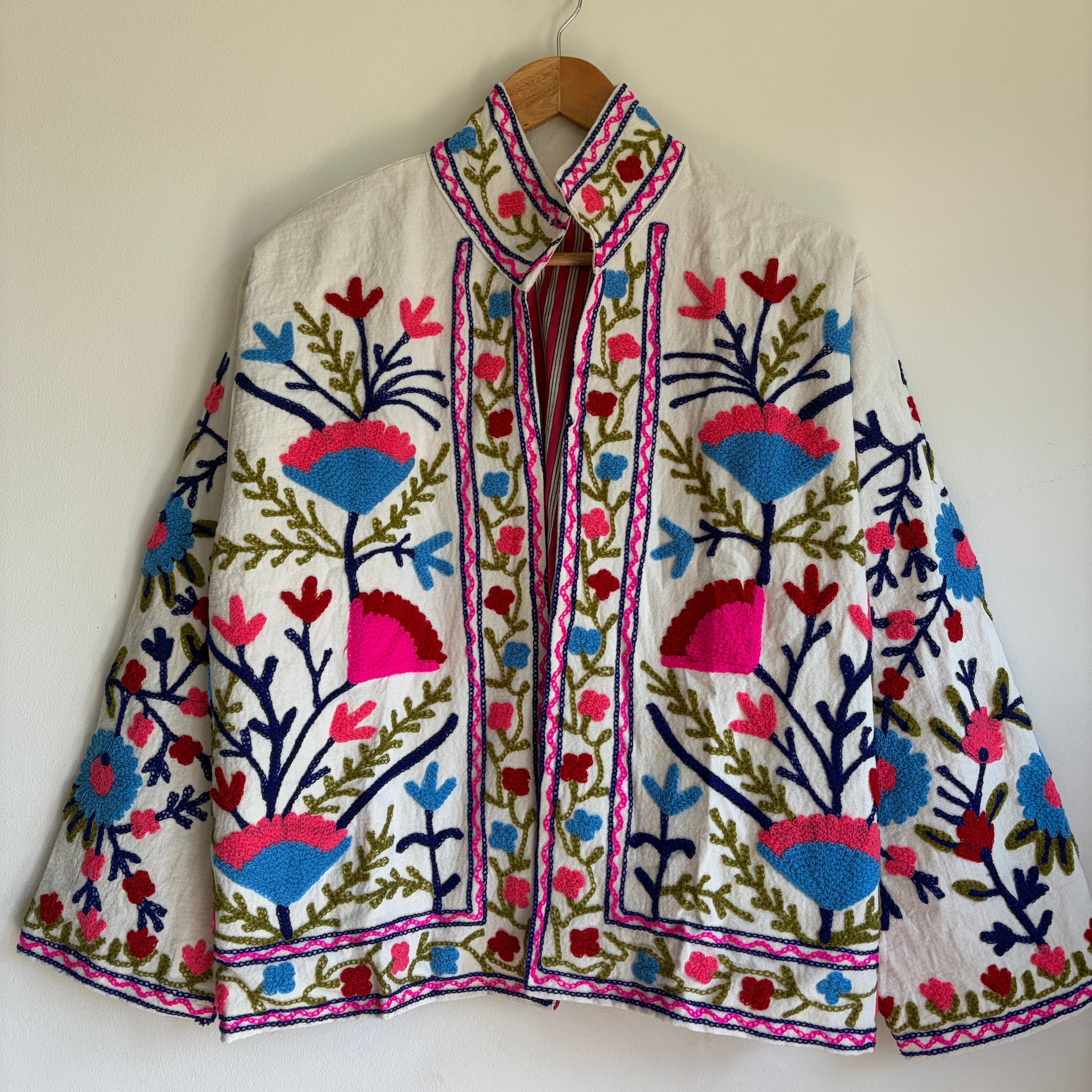 Colorful embroidered jacket on a hanger against a white background