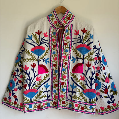 Colorful embroidered jacket on a hanger against a white background