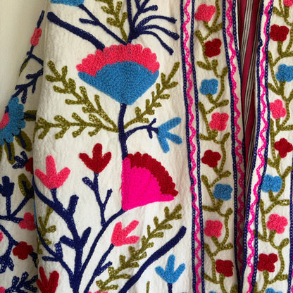 Colorful embroidered jacket on a hanger against a white background