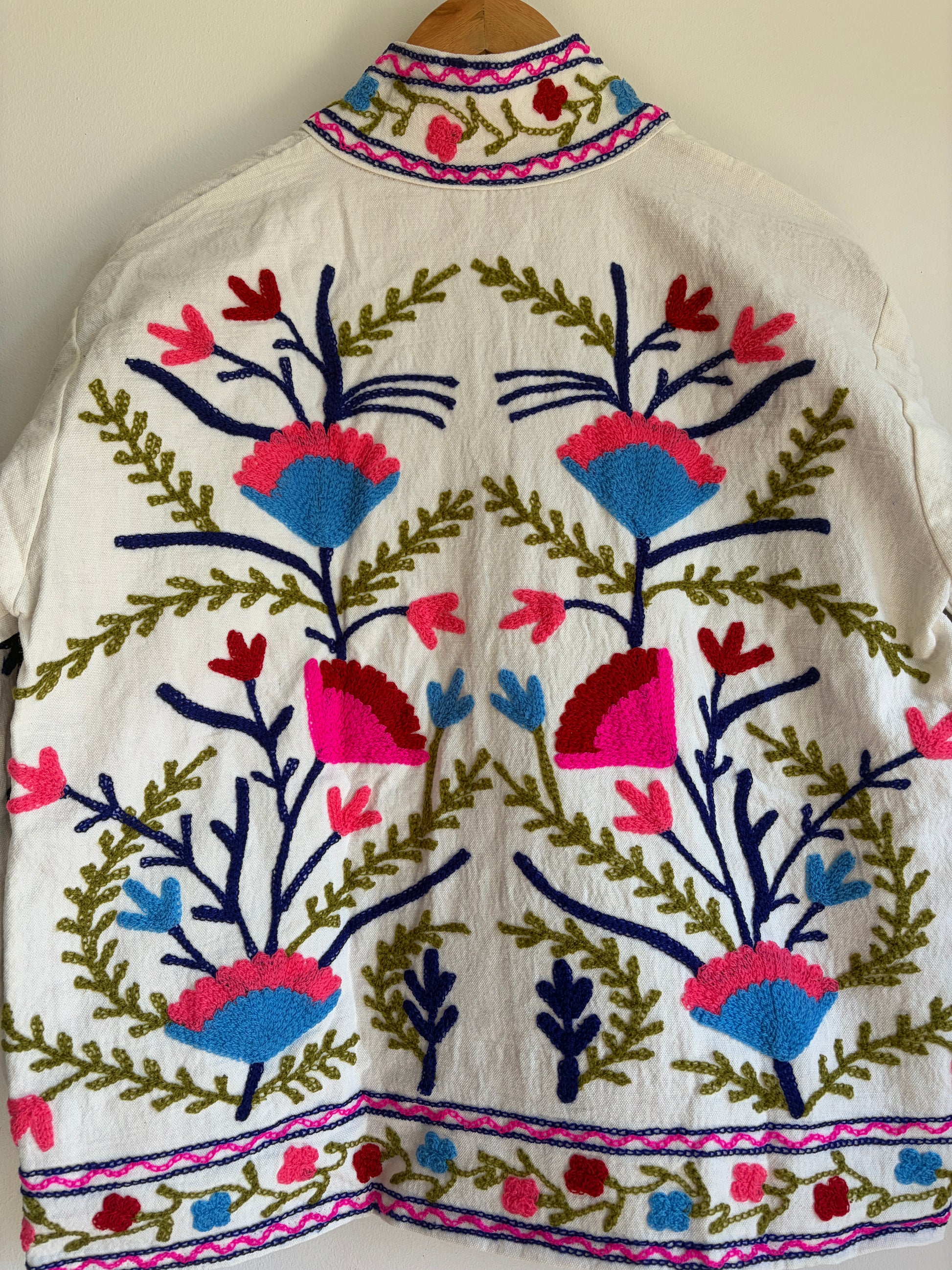 Colorful embroidered jacket on a hanger against a white background