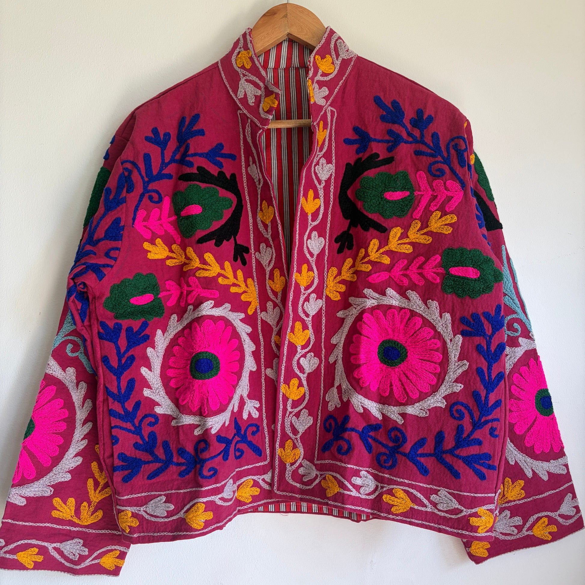Colorful embroidered jacket on a hanger against a white background