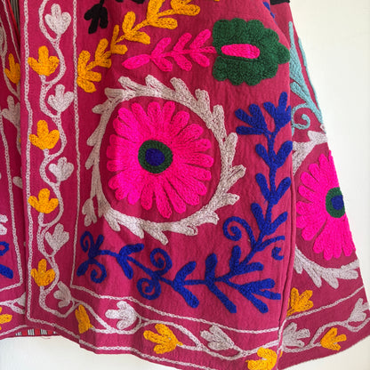 Colorful embroidered jacket on a hanger against a white background