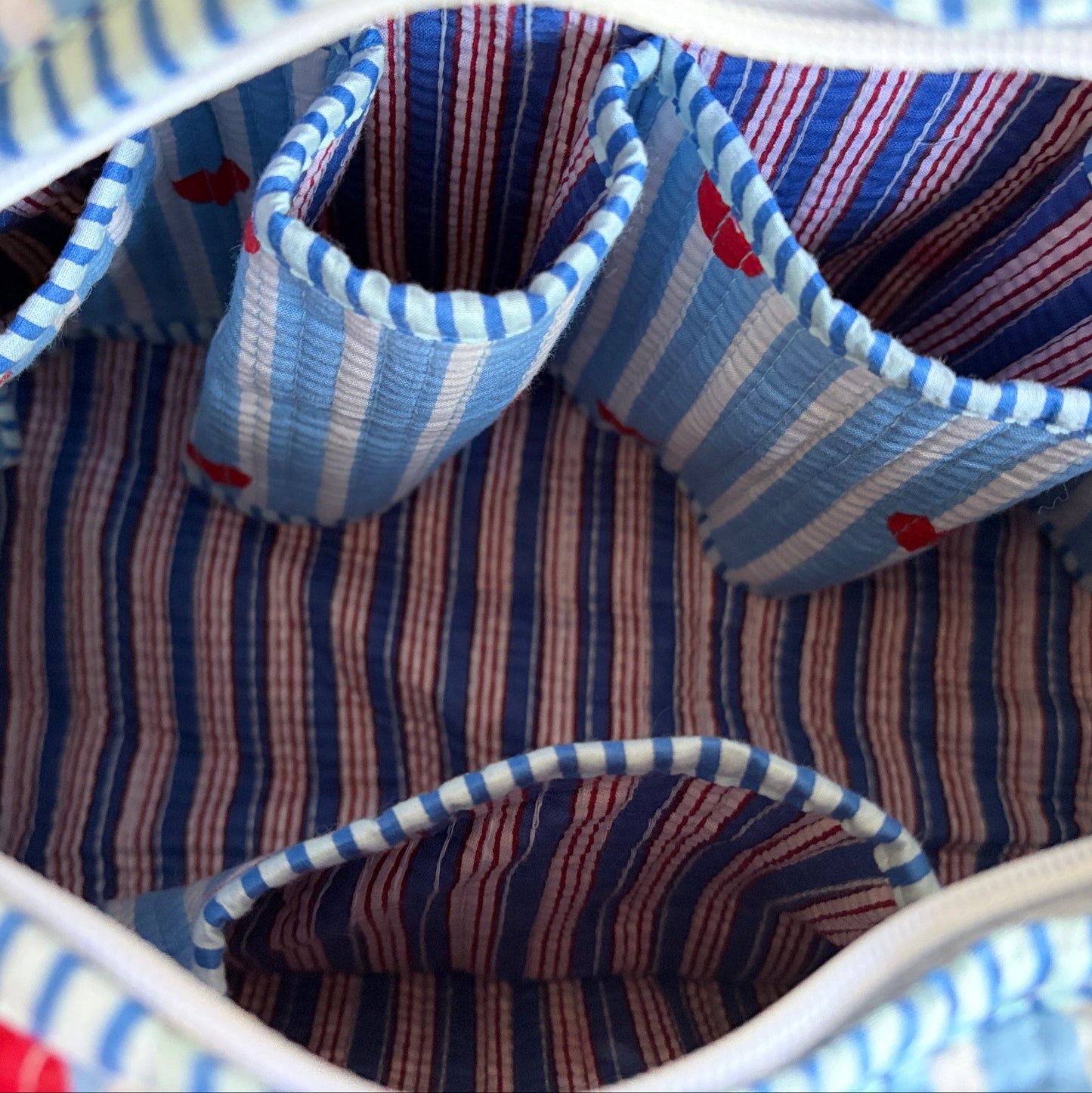 Quilted cotton make up bag with a blue and white striped pattern and red heart motifs.