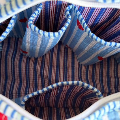 Quilted cotton make up bag with a blue and white striped pattern and red heart motifs.