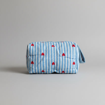 Quilted cotton make up bag with a blue and white striped pattern and red heart motifs.
