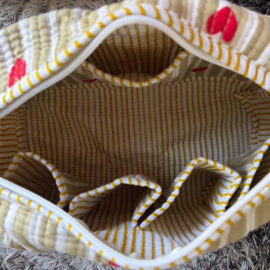 Close-up of the inside of a quilted fabric tote bag with yellow and white stripes, cream borders, and small red floral accents, photographed on a textured gray surface.