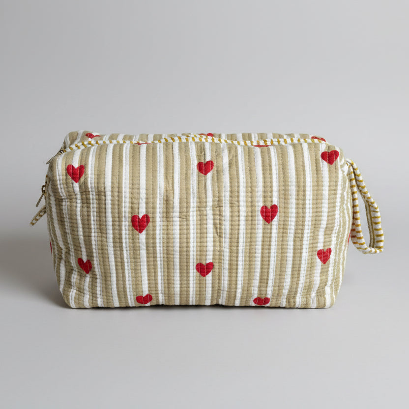 A rectangular zippered storage bag or organizer cover with vertical cream and olive stripes and red heart motifs, resting on a teal upholstered stool in an indoor room.