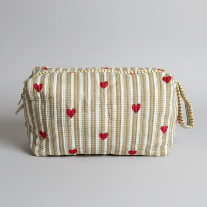 A rectangular zippered storage bag or organizer cover with vertical cream and olive stripes and red heart motifs, resting on a teal upholstered stool in an indoor room.