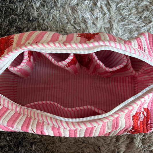 Pink and white striped fabric zippered pouch with multiple interior pockets, photographed from above on a shaggy gray rug.
