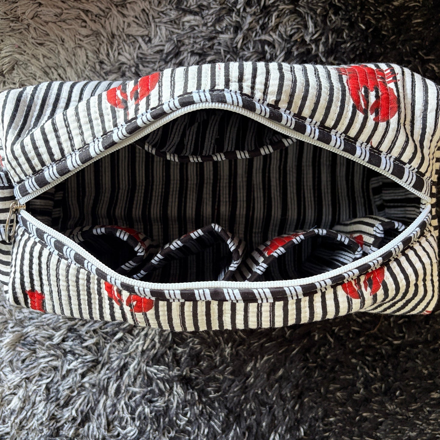 A striped fabric make up bag with red lobster prints.