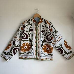 white cotton jacket with a colorful suzani embroidered floral and geometric pattern in brown, orange, and green. 