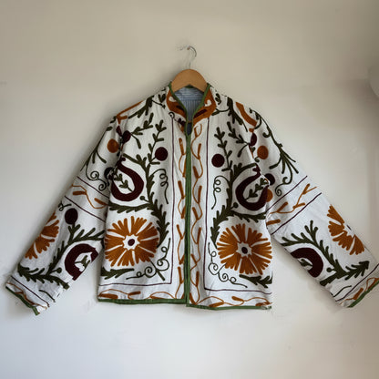white cotton jacket with a colorful suzani embroidered floral and geometric pattern in brown, orange, and green. 