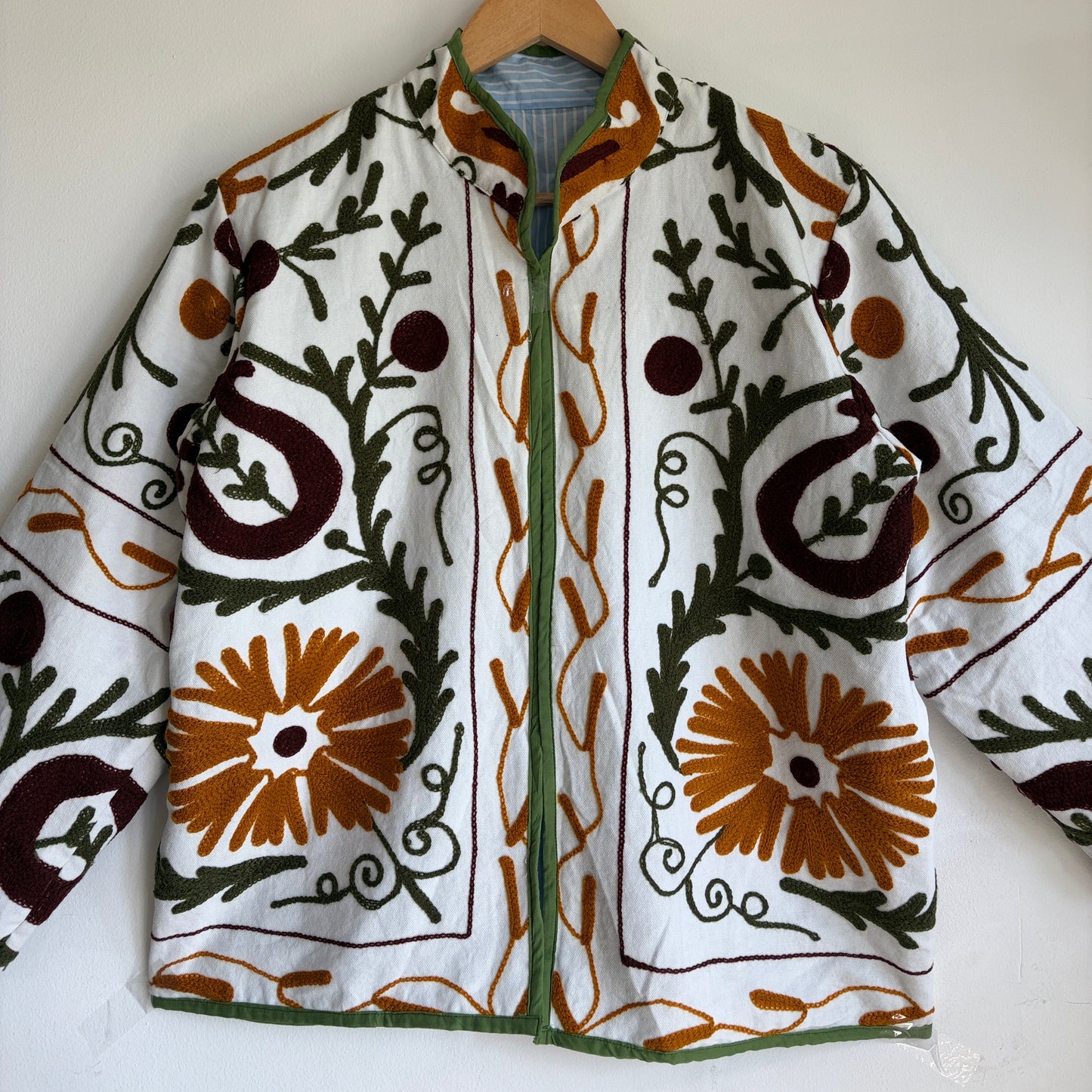 white cotton jacket with a colorful suzani embroidered floral and geometric pattern in brown, orange, and green. 