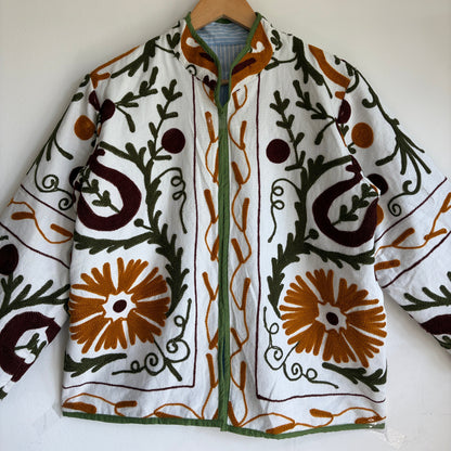 white cotton jacket with a colorful suzani embroidered floral and geometric pattern in brown, orange, and green. 