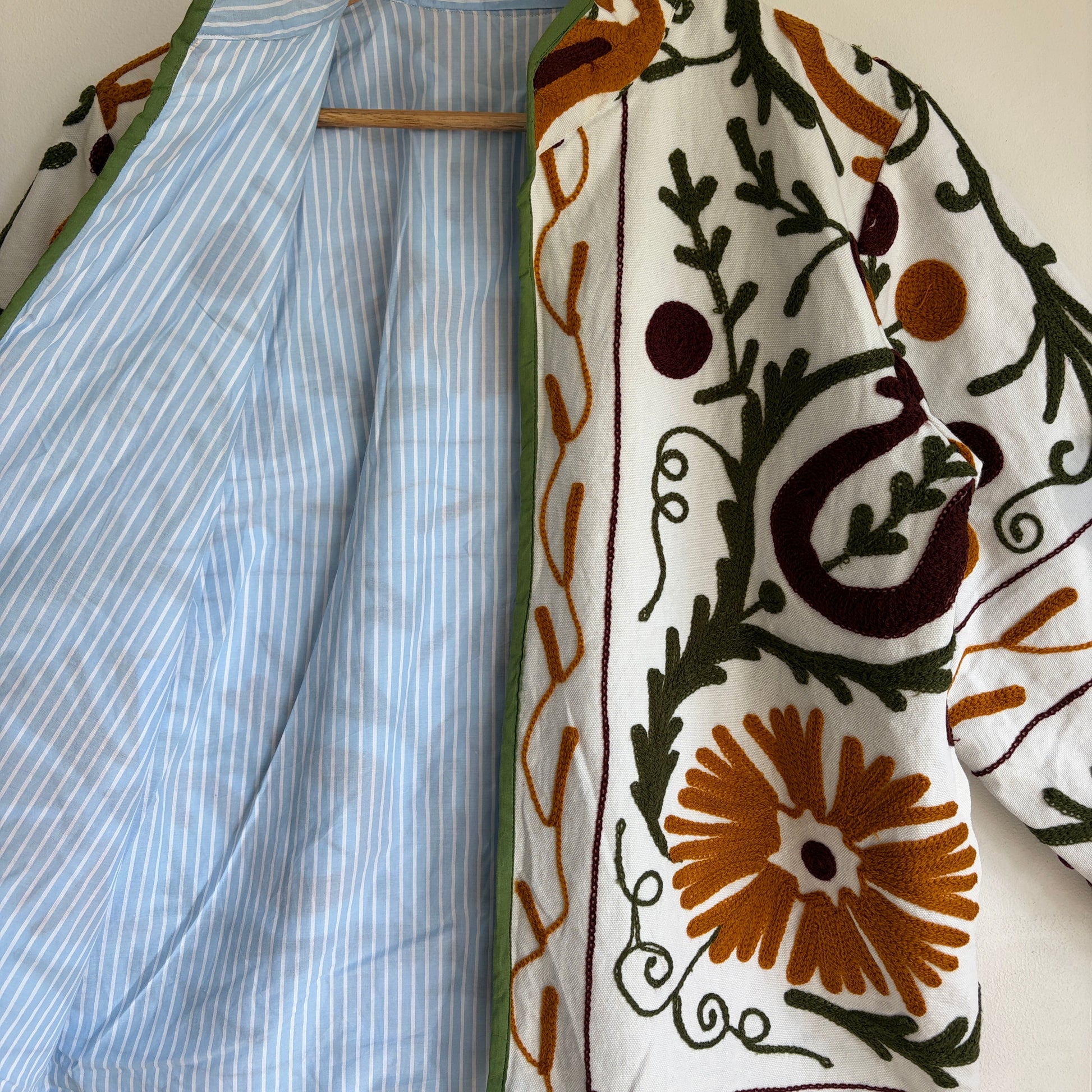 white cotton jacket with a colorful suzani embroidered floral and geometric pattern in brown, orange, and green. 