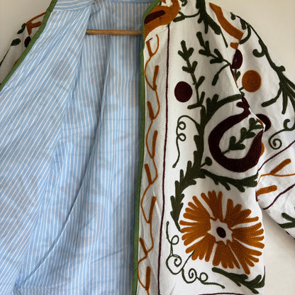 white cotton jacket with a colorful suzani embroidered floral and geometric pattern in brown, orange, and green. 