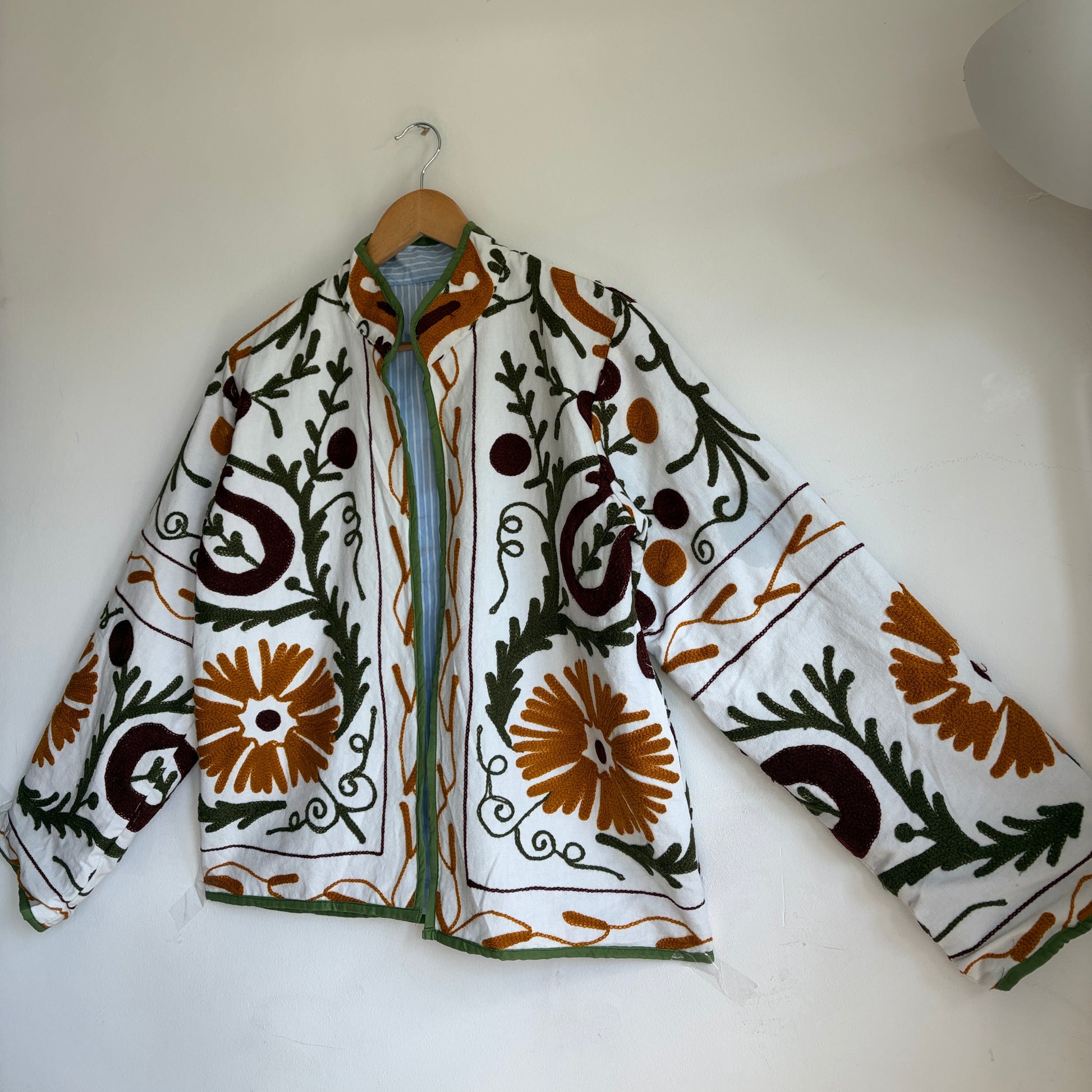 white cotton jacket with a colorful suzani embroidered floral and geometric pattern in brown, orange, and green. 