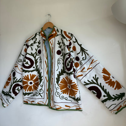 white cotton jacket with a colorful suzani embroidered floral and geometric pattern in brown, orange, and green. 